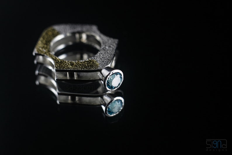 Contemporary ring with reticulated sterling silver and keum boo 24k gold foil and blue topaz stone, double-sided. On Mirror, Black Background.