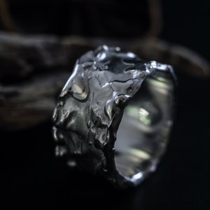 Molten Metal Chunky Ring, Dramatic Jewellery for Men and Women, Unisex Broad Ring with Irregular Edges. On Black Background with Dry Cactus Wood Behind.