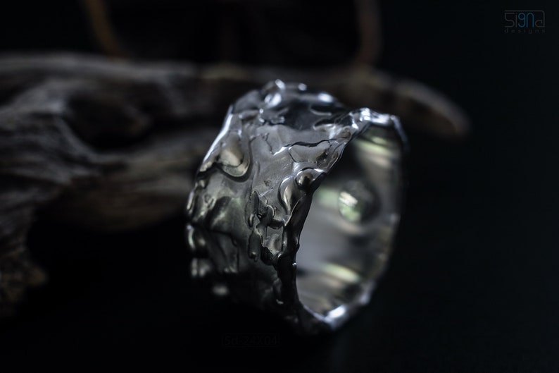 Molten Metal Chunky Ring, Dramatic Jewellery for Men and Women, Unisex Broad Ring with Irregular Edges. On Black Background with Dry Cactus Wood Behind.