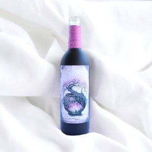 May include: A dark glass wine bottle with a pink ribbon around the neck. The label features a watercolor painting of a bonsai tree with pink blossoms.