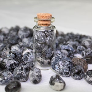 May include: A small glass bottle with a cork stopper filled with black and white agate stones. The bottle is surrounded by loose black and white agate stones.