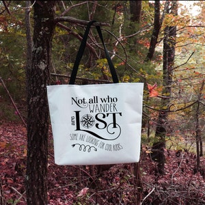 May include: White canvas tote bag with black straps and a black graphic that reads "Not all who wander are lost. Some are looking for cool rocks."