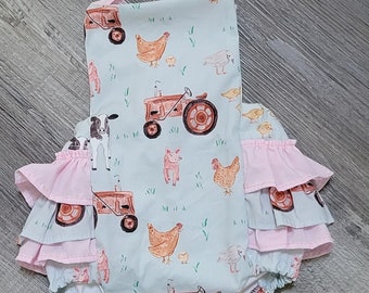 May include: A light blue baby onesie with a pink ruffle trim. The onesie features a farm-themed print with tractors, chickens, pigs, and cows.