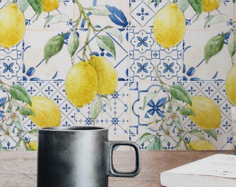 Op de afbeelding: Een zwarte keramische mok staat op een houten tafel voor een betegelde muur met een citroenboomontwerp. De tegels zijn wit met blauwe en gele accenten.