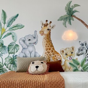 May include: A white bed with a brown knitted blanket and a lion-shaped pillow. The wall behind the bed has a jungle theme with a giraffe, elephant, lion, zebra, and palm trees.