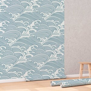 May include: A roll of blue and white patterned wallpaper with a wave design. The wallpaper is partially unrolled and is lying on a wooden floor. A small wooden stool is in the background.