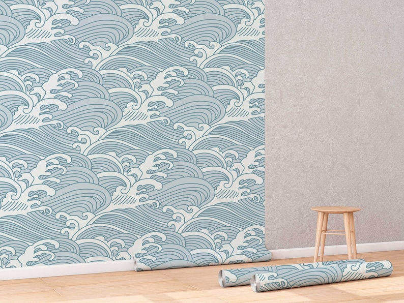 May include: A roll of blue and white patterned wallpaper with a wave design. The wallpaper is partially unrolled and is lying on a wooden floor. A small wooden stool is in the background.