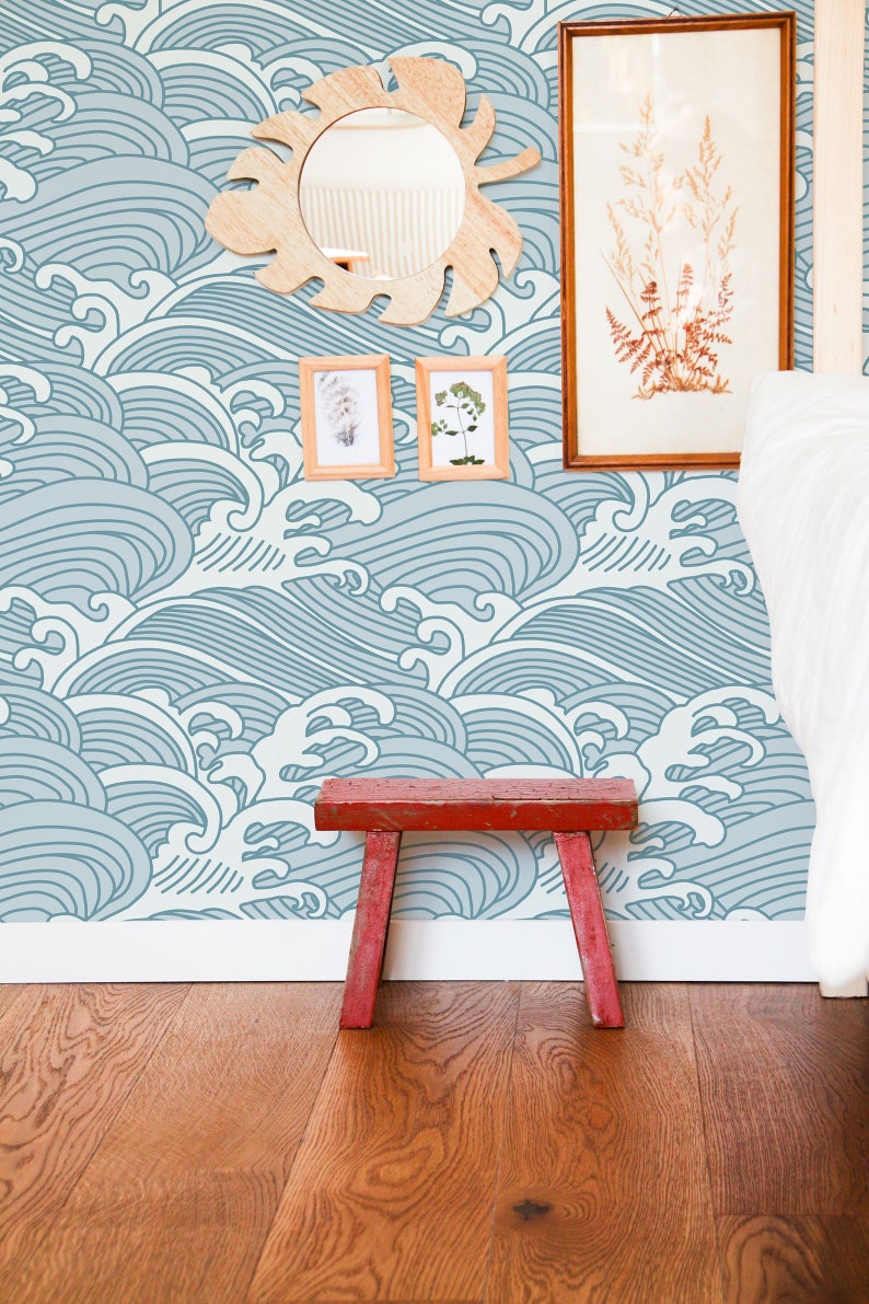 May include: A blue and white wave pattern wallpaper with a wooden mirror, two framed pictures, and a red wooden stool in front of it.