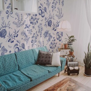 May include: A teal blue sofa with two pillows sits in a living room with white walls and a blue and white floral wallpaper. A potted plant is in the corner of the room.
