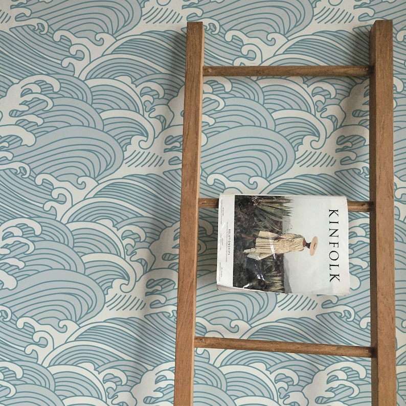 May include: A wooden ladder leaning against a wall covered in blue and white wave patterned wallpaper. A magazine titled "Kinfolk" is resting on the ladder.