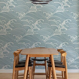 May include: A wooden dining table with four chairs. The table and chairs are made of light wood. The chairs have black cushions. The wall behind the table is covered in a blue and white wave pattern wallpaper.