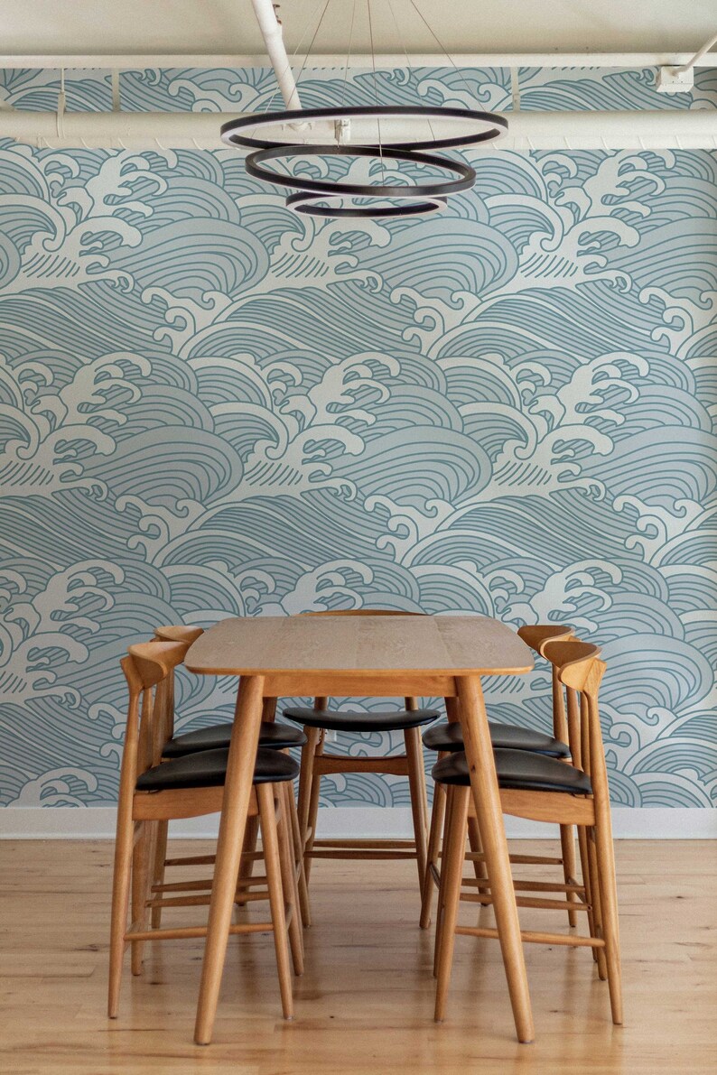 May include: A wooden dining table with four chairs. The table and chairs are made of light wood. The chairs have black cushions. The wall behind the table is covered in a blue and white wave pattern wallpaper.