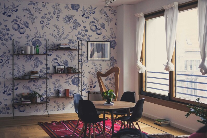 May include: A dining room with a floral wallpaper, a harp, a table with four chairs, and a bookshelf. The table is made of wood and has a round top. The chairs are black and have a wooden frame. The bookshelf is made of metal and has four shelves. The harp is made of wood and has a gold finish.