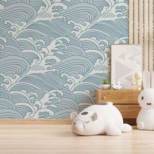 May include: A light blue and white wave patterned wallpaper with a wooden shelf and a variety of stuffed animals, including a white polar bear, a white rabbit, and a gray pineapple with glasses.