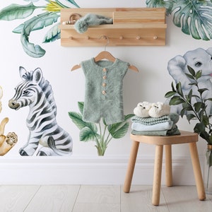 May include: A nursery wall decal set featuring a zebra, lion, giraffe, elephant, and palm trees. The decals are in a watercolour style and are perfect for a jungle-themed nursery.