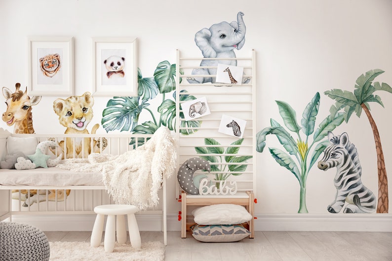 May include: A nursery room decorated with jungle animal wall decals. The decals feature a giraffe, lion, elephant, zebra, and palm trees. The decals are in a watercolour style and are a light blue, green, and brown colour.
