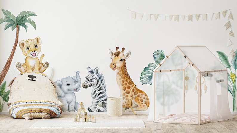 May include: A nursery room with a white wall decorated with a jungle animal theme. The wall has a palm tree, a lion, a zebra, a giraffe, and an elephant. There is a white play tent with a pink blanket inside. The room has a wooden floor and a white rug.