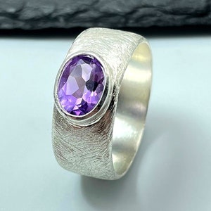 Könnte beinhalten: Ein silberner Ring mit einer strukturierten Band und einem violetten Amethyst-Edelstein.