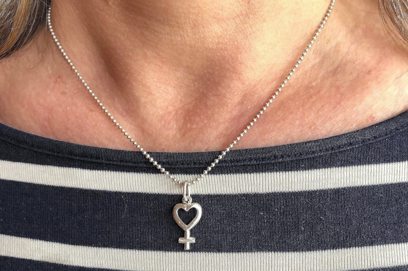 May include: A silver necklace with a heart-shaped pendant featuring the female symbol.