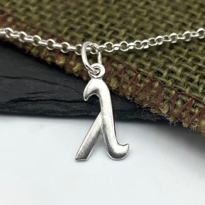K&ouml;nnte beinhalten: Eine silberne Kettenkette mit einem silbernen Anh&auml;nger in Form des Buchstabens Lambda.
