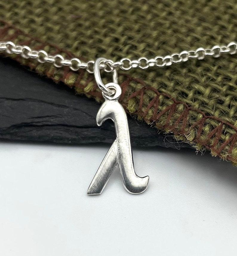 K&ouml;nnte beinhalten: Eine silberne Kettenkette mit einem silbernen Anh&auml;nger in Form des Buchstabens Lambda.