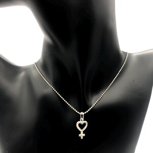 May include: A silver necklace with a heart-shaped pendant featuring the female symbol.
