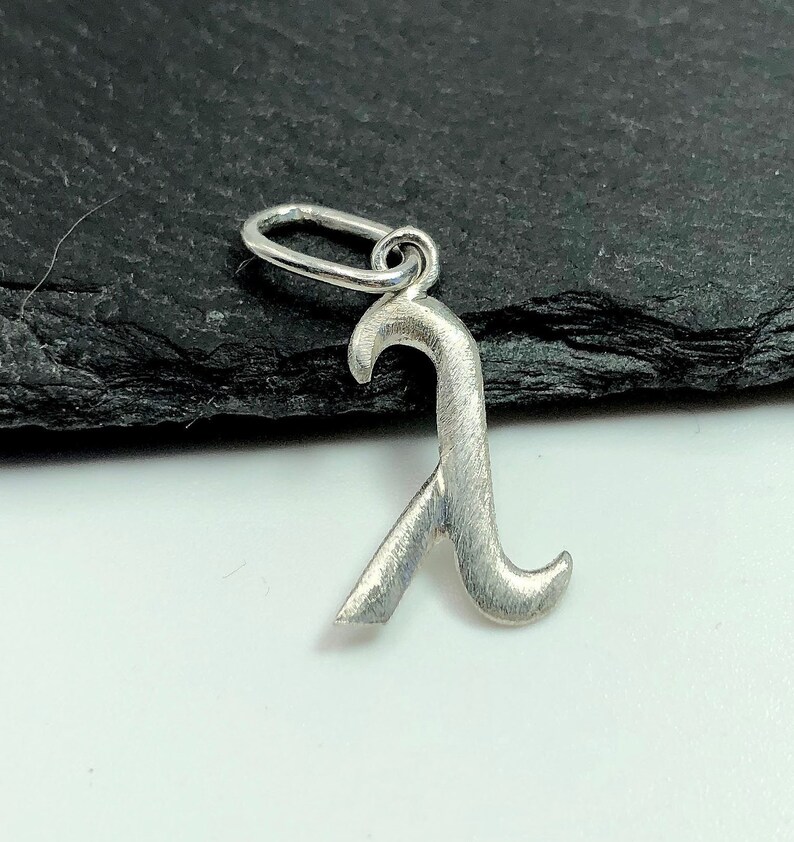 K&ouml;nnte beinhalten: Ein silberner Anh&auml;nger in Form des Buchstabens "R" mit geb&uuml;rsteter Oberfl&auml;che. Der Anh&auml;nger hat oben eine &Ouml;se zum Anbringen an einem Armband oder einer Halskette.