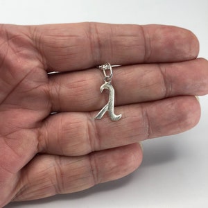 K&ouml;nnte beinhalten: Silberner Anh&auml;nger in Form des Buchstabens 'A' mit einem dekorativen, stilisierten Design. Der Anh&auml;nger h&auml;ngt an einer silbernen Kette.