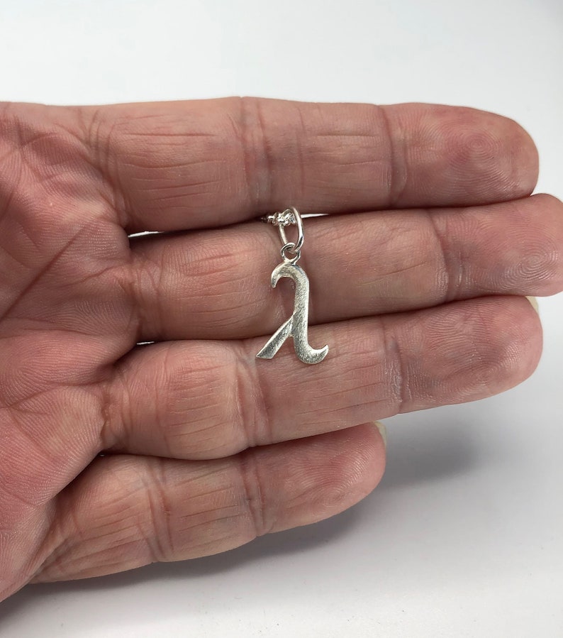 K&ouml;nnte beinhalten: Silberner Anh&auml;nger in Form des Buchstabens 'A' mit einem dekorativen, stilisierten Design. Der Anh&auml;nger h&auml;ngt an einer silbernen Kette.