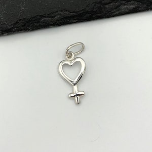 May include: A silver charm in the shape of a heart with a female symbol inside.
