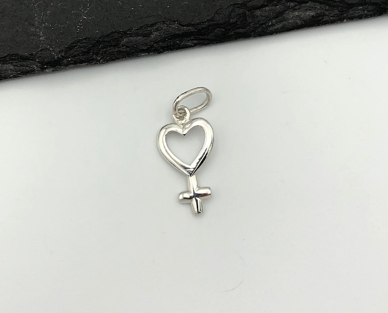 May include: A silver charm in the shape of a heart with a female symbol inside.
