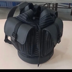 May include: A black and white striped backpack with black leather accents and buckles. The backpack has a unique design that resembles a vest.