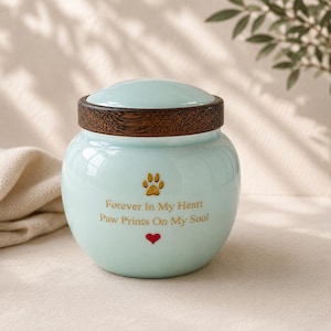 Peut inclure: Une urne en c&eacute;ramique bleu clair avec un couvercle en bois brun fonc&eacute;. L'avant pr&eacute;sente une empreinte de patte dor&eacute;e, le texte "Forever In My Heart Paw Prints On My Soul" en lettres dor&eacute;es et un petit c&oelig;ur rouge sous le texte.