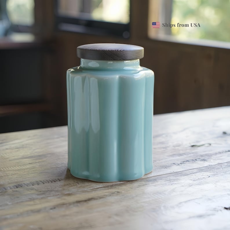 May include: A light blue ceramic jar with a wooden lid. The jar has a ribbed design and a glossy finish. The lid is made of wood and fits snugly on top. The jar is sitting on a wooden surface.