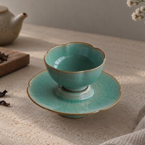May include: A light turquoise ceramic tea cup and matching saucer set featuring a scalloped edge design and a visible crackle glaze finish. The rim of both the cup and the saucer is accented with a thin, metallic gold-toned trim.