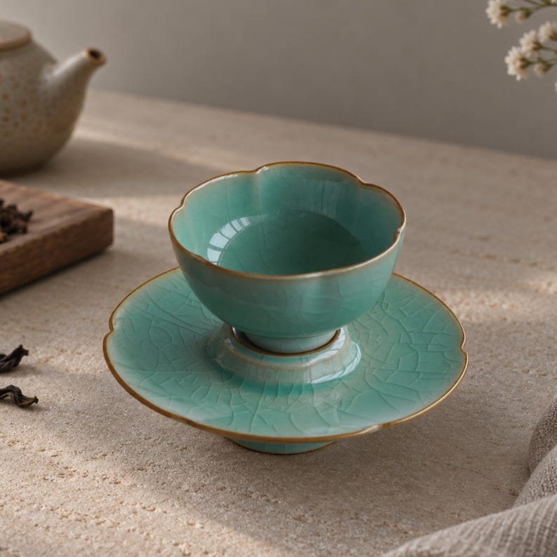 May include: A light turquoise ceramic tea cup and matching saucer set featuring a scalloped edge design and a visible crackle glaze finish. The rim of both the cup and the saucer is accented with a thin, metallic gold-toned trim.