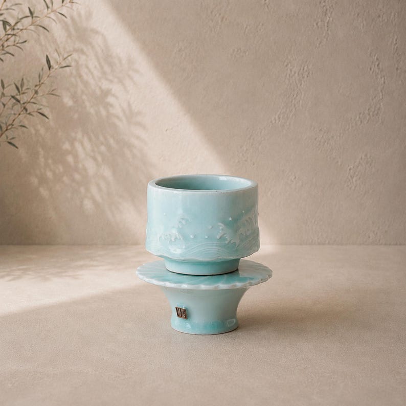 May include: A light blue ceramic cup and saucer set. The cup has a textured wave design around the top. The saucer has a scalloped edge. The set is on a neutral background with shadows.