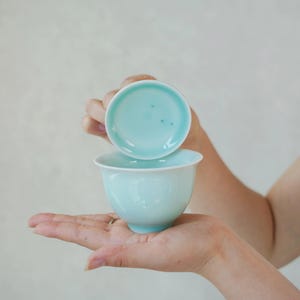 K&ouml;nnte beinhalten: Eine hellt&uuml;rkisfarbene Teetasse aus Keramik mit passender Untertasse. Die Tasse hat eine glatte, abgerundete Schalenform und eine gl&auml;nzende Oberfl&auml;che, w&auml;hrend die Untertasse eine leicht konkave Mitte und einen klaren, kreisf&ouml;rmigen Rand aufweist.