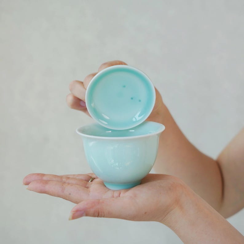 K&ouml;nnte beinhalten: Eine hellt&uuml;rkisfarbene Teetasse aus Keramik mit passender Untertasse. Die Tasse hat eine glatte, abgerundete Schalenform und eine gl&auml;nzende Oberfl&auml;che, w&auml;hrend die Untertasse eine leicht konkave Mitte und einen klaren, kreisf&ouml;rmigen Rand aufweist.