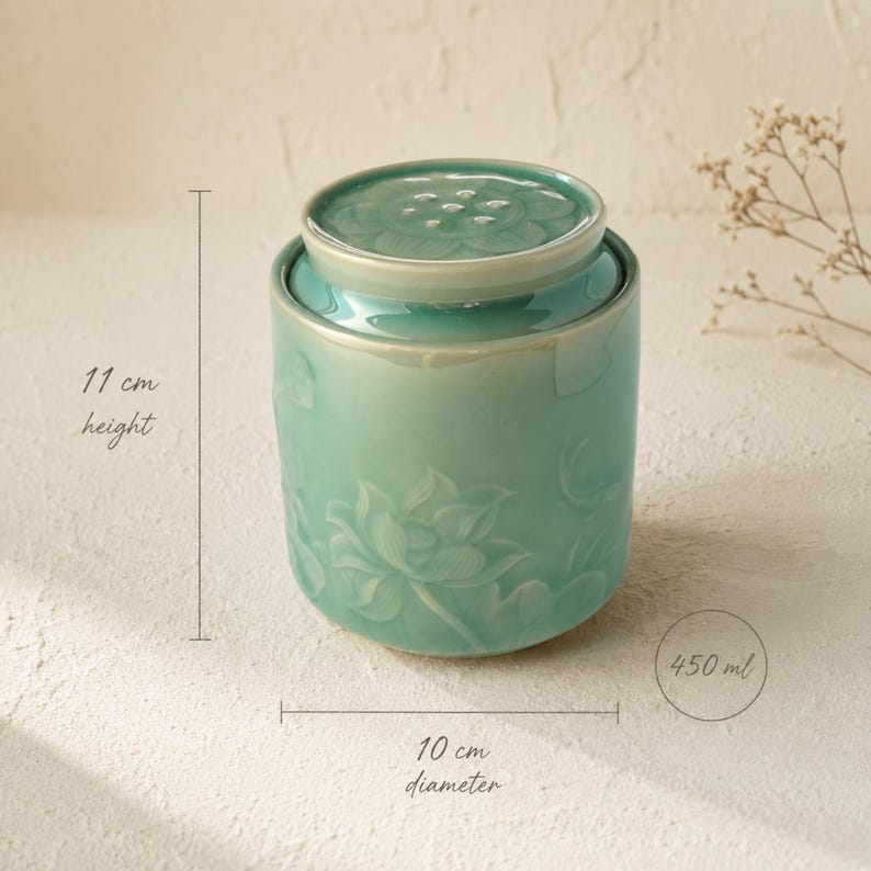 May include: A cylindrical light green ceramic jar with a matching lid, featuring a relief lotus flower design. The jar has a height of 11 cm, a diameter of 10 cm, and a capacity of 450 ml, as indicated by the text labels on the image.