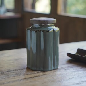 May include: A teal ceramic jar with a ribbed design and a wooden lid. The jar is cylindrical with a slightly flared base and a wooden lid. The jar is sitting on a wooden table.