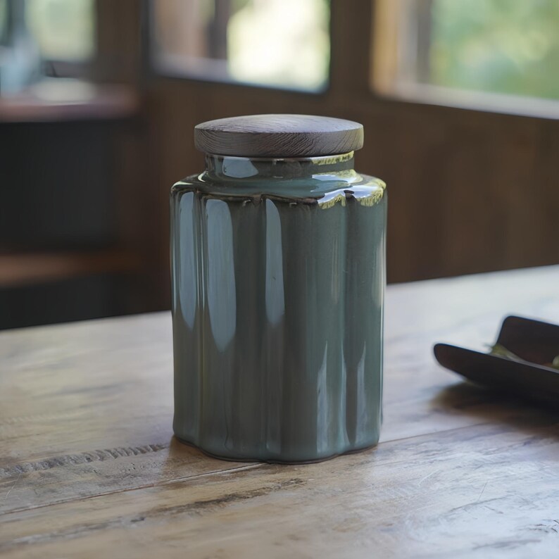 May include: A teal ceramic jar with a ribbed design and a wooden lid. The jar is cylindrical with a slightly flared base and a wooden lid. The jar is sitting on a wooden table.