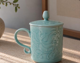 May include: A light blue ceramic mug with a matching lid, featuring an embossed floral pattern across the exterior. The mug has a curved handle with a small loop at the base and a smooth, glossy finish that reflects light across its surface.