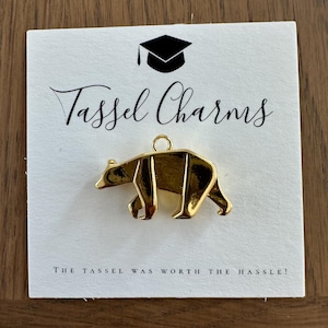 Könnte beinhalten: Goldfarbener Bären-Anhänger mit einem Abschluss-Hut-Symbol und dem Text "Tassel Charms" und "The tassel was worth the hassle!"