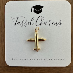 May include: Gold airplane tassel charm with the text "Tassel Charms" and "The tassel was worth the hassle!" on a white card with a black graduation cap icon.