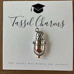 Peut inclure: Breloque en argent pour pompon en forme de microphone vintage. Le breloque est sur une carte blanche avec le texte "Tassel Charms" et "The tassel was worth the hassle!"