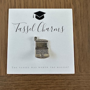 May include: A silver charm in the shape of a laptop computer. The charm is on a white card with the text "Tassel Charms" and "The tassel was worth the hassle!"