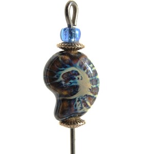 May include: A handcrafted bead featuring a nautilus shell design. The bead is primarily dark blue and brown with lighter blue and tan accents. It is topped with a small blue bead and a silver-colored loop, mounted on a silver pin.