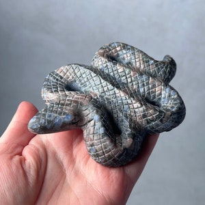 May include: A hand-carved stone snake sculpture with a blue, gray, and brown mottled pattern. The snake is curled up in a coil.