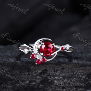 May include: A silver ring with a red ruby gemstone and smaller ruby accents. The ring features a crescent moon design.